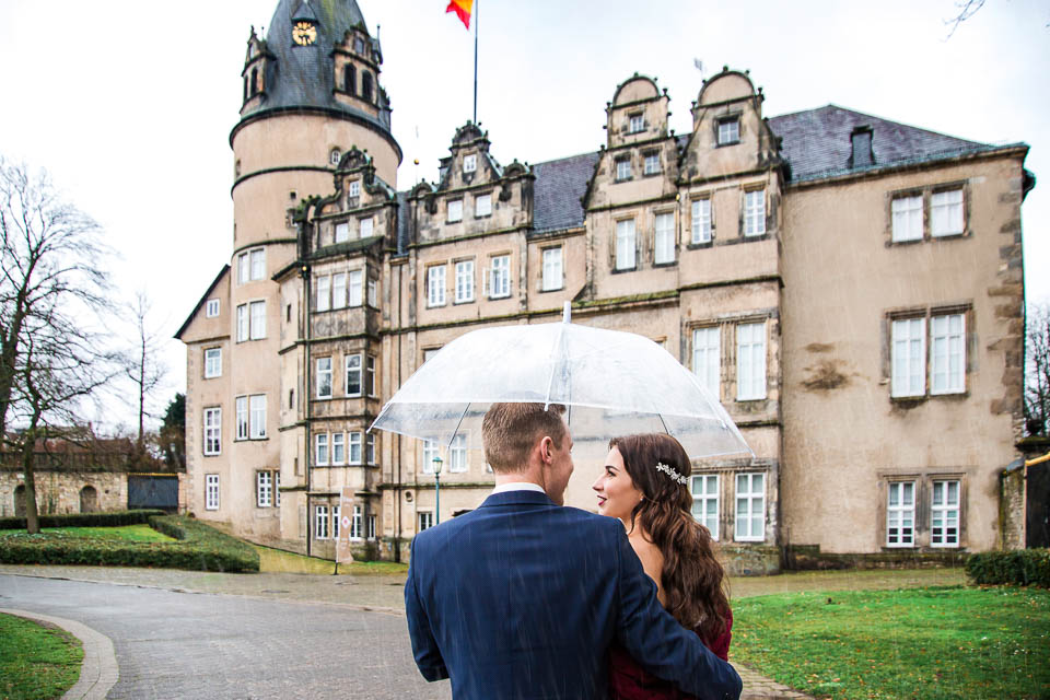 Brautpaar unter Regenschirm vor Schloss
