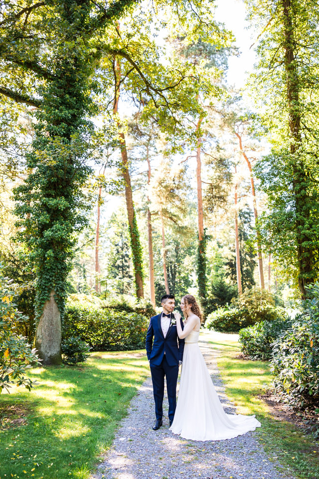 Das internationale Brautpaar posiert beim Hochzeits-Shooting in Bielefeld. Sie befinden sich in einem sehr grünbewachsenen Park. Die Kulisse ähnelt einem Märchenwald.