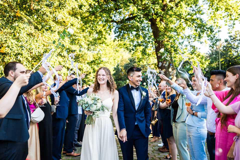 Die Hochzeitsgäste empfangen das glückliche Brautpaar mit einem Spalier aus wehenden Bändern und Seifenblasen auf Hof Steffen in Bielefeld.