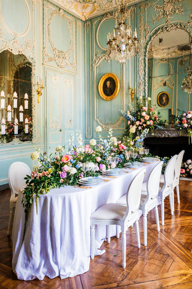 Uppig dekorierte Hochzeitstafel im Festsaal eines französischen Schlosses. Große Spiegel und Ölgemälde zieren die hellblauen Wände.