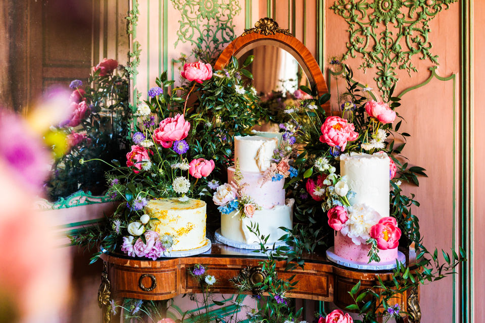 Drei pastellige Hochzeitstorten auf antikem Spiegeltisch, umringt von französischen Blumenarrangements.