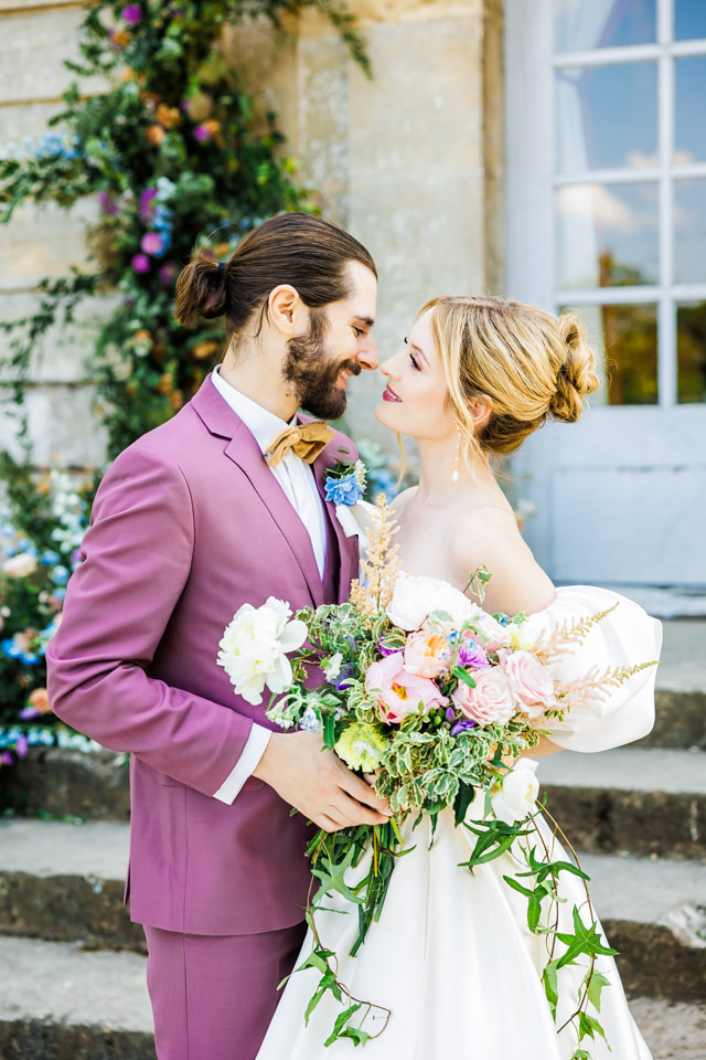 Französisch inspiriertes Hochzeits-Shooting. Die Braut trägt ein schulterfreies Kleid, der Bärutigam einen violetten Anzug.