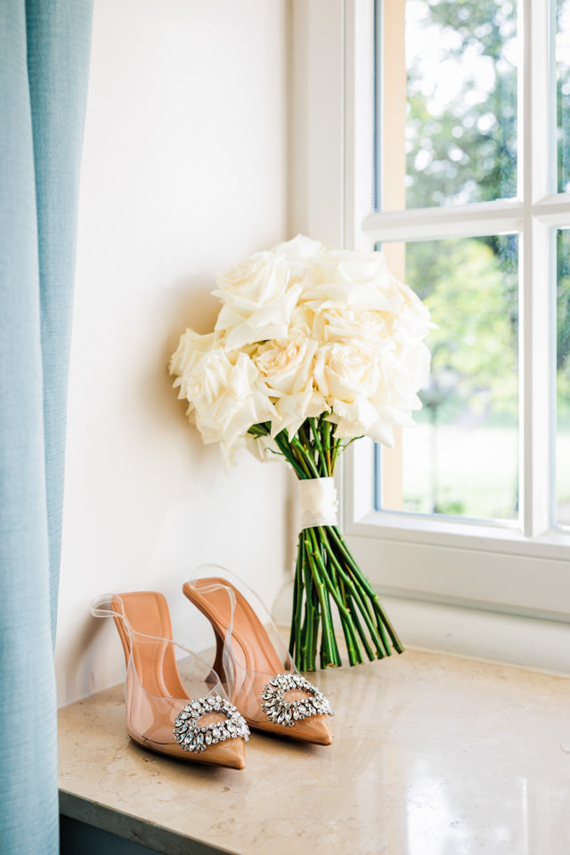 Ein weißer Brautstrauß und funkelnde Brautschuhe stehen schön drapiert in einer hellen Fensterniesche beim Getting Ready in der Klosterpforte Marienfeld.