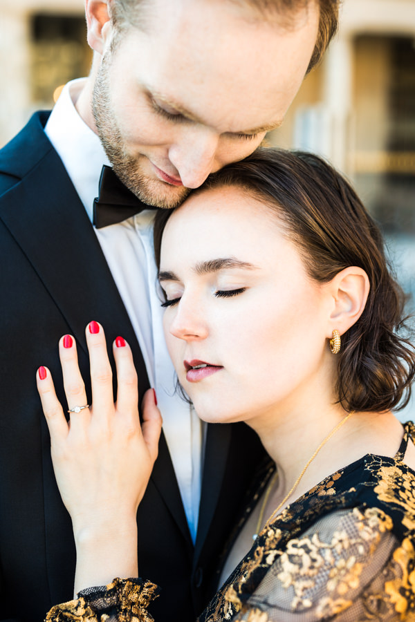 Paar lehnt sich aneinander an, hat die Augen zu und genießt die Zweisamkeit beim Verlobungsshooting. Ihre Hand mit Verlobungsring ruht auf seinem Sakko.