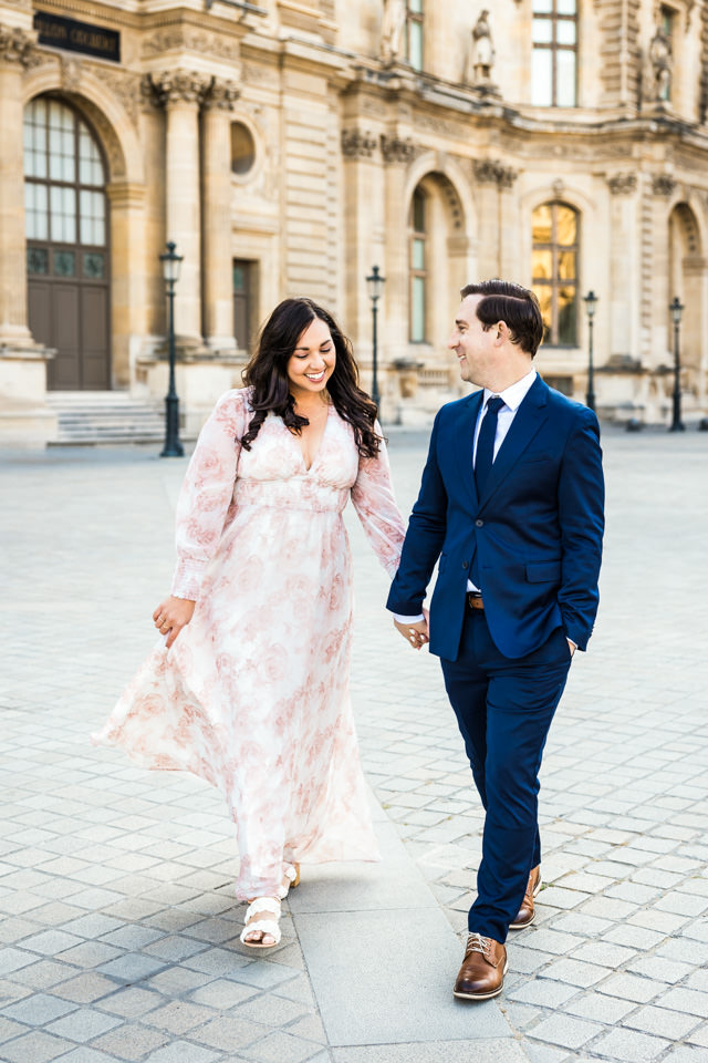 Paar spaziert beim Paarshooting durch Paris. Sie trägt ein florales Kleid und er einen blauen Anzug.